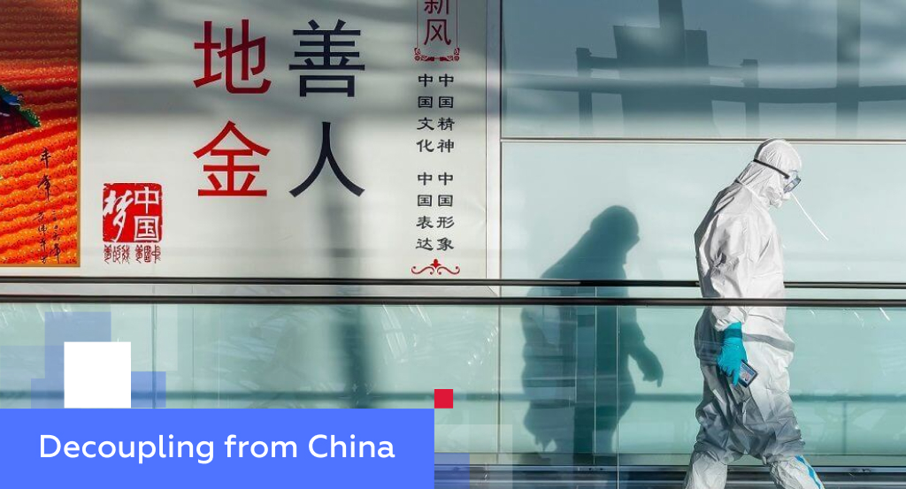 Worker in a white hazmat suit beside Chinese cultural posters — illustrating decoupling from China